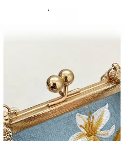Detail of light blue embroidered floral fabric and vintage golden ball clasp on a bag