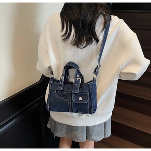 Detailed view of dark blue denim crossbody bag featuring vintage metal buckles and stitching