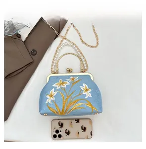 Detail of vintage sky blue embroidered handbag with pearl handle and floral gold patterns