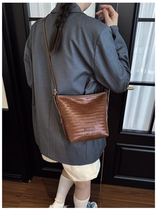 Close-up of brown woven leather bucket bag with metal logo detail on model