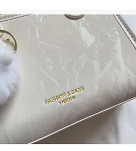 Détail du sac à main crème motif marbre avec logo doré et pendentif en peluche