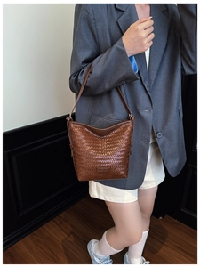 Detail view of brown woven bucket bag with leather strap and texture on model