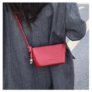 Detail of red leather crossbody bag with silver heart charm on model in gray suit
