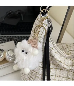 Close-up of white plush monster keychain with pink knit hat on a woven bag