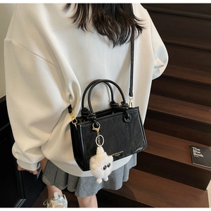 Close-up of black pleated PU leather bucket bag with gold hardware and plush charm
