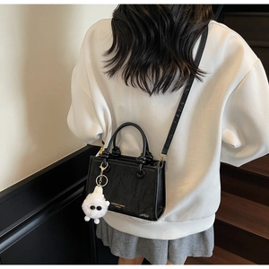 Detail of black textured crossbody bag featuring fashion print and plush monster charm