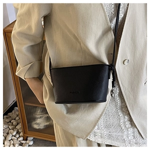 Detail of black pebbled leather crossbody bucket bag with FASHION logo and slim strap