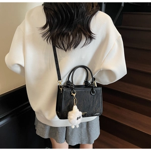 Detail of a black textured leather bucket bag with gold hardware and white plush charm