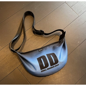 Top view of a crescent-shaped nylon crossbody bag featuring a blue gradient and DD print