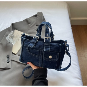 Close-up of deep blue denim tote bag with silver buckles and multi-pocket design on white linen