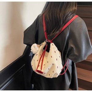 Detail of cream canvas backpack with red bows and plush toy on wooden stairs