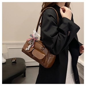 Detail of dark brown retro shoulder bag with decorative flap pockets and bow ribbon charm