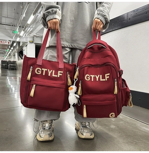 Detail of burgundy canvas backpack and tote set with beige GTYLF letter patches