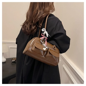 Detail of brown patent leather underarm bag with decorative ribbon and heart pendant charm