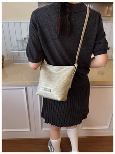 Detail of light gold woven crossbody bucket bag with textured finish on a female model