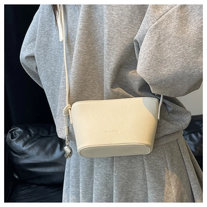 Detail of off-white lychee leather mini crossbody bag with silver bean charm and knot strap