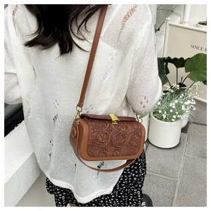 Outdoor street style shot of brown floral embossed cylinder crossbody bag on model