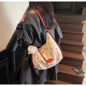 Detail of canvas hobo bag with red bow print and plush lamb charm on a shoulder strap