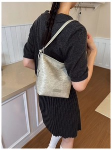 Detail showing woven texture and gold metal logo plate on champagne bucket bag