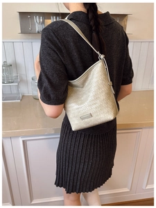 Detail of champagne gold woven shoulder bag with metallic logo plate on kitchen counter