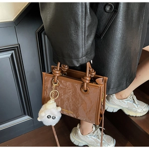 Close-up of pleated leather bucket bag with knotted handle and white plush charm detail