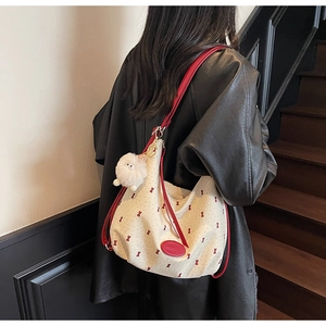 Detail of cream hobo bag with red bow patterns and fluffy ball charm on model
