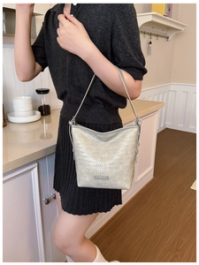 Detail of champagne gold woven texture bucket bag with metallic logo and thin leather strap