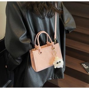 Detail of pink faux leather crossbody bag with white pompom charm and top handles
