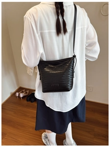 Detail view of black woven crossbody bucket bag with adjustable leather strap worn by a model