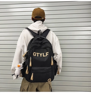 Detail view of black nylon backpack featuring GTYLF letter print and white duck pendant