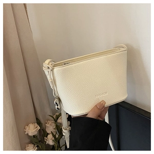 Close-up of beige lychee grain leather crossbody bag with silver heart pendant detail