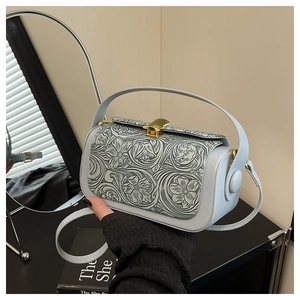 Detail of light blue crossbody bag featuring floral embossed pattern and gold shell clasp