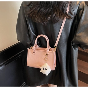 Pink faux leather bucket bag with plush charm and gold hardware on black leather jacket