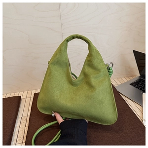 Close-up of green suede triangle crossbody bag with round handle and leather strap