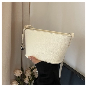 Detail of creamy white crossbody bag showing lychee leather texture and heart charm