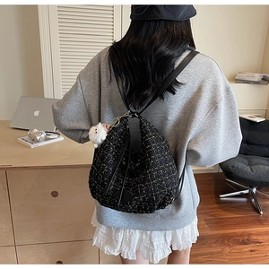 Detail of black tweed backpack with gold accents and plush charm on a model