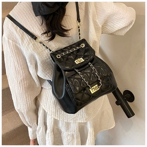 Detail of a quilted black leather mini backpack with gold chains on a white dress model