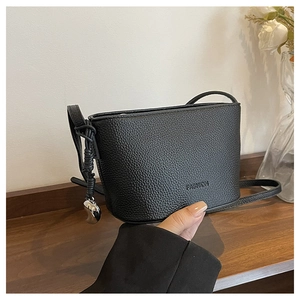 Detail of black litchi grain bucket bag with FASHION embossment and silver heart charm