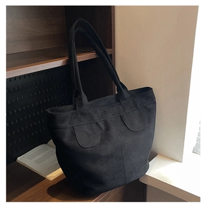 Detailed view of black suede tote bag with decorative patches on wooden shelf