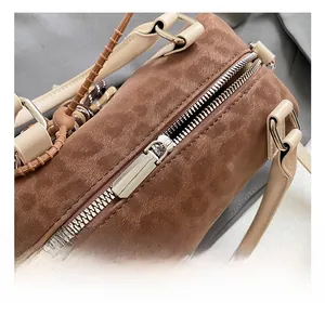 Detail of silver hardware and smooth zipper on brown suede Boston bag with beige handles