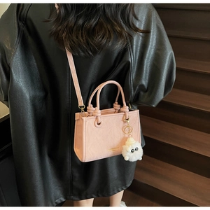 Sac seau en cuir rose avec breloque en peluche porté sur une veste noire élégante