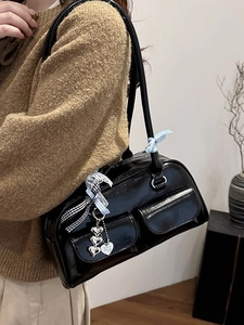 Glossy black underarm bag with front pockets and bow detail worn over the shoulder
