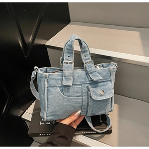 Macro detail of light blue denim tote with silver metal buckles and textured fabric