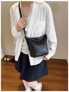 Detail of a black woven bucket bag on a model wearing white lace and a black skirt