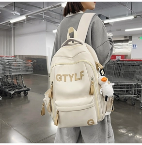Detail of a beige nylon backpack with a cute duck pendant worn in a casual store setting