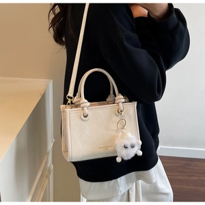 Detailed view of a white mini tote bag featuring a plush monster charm and top handles