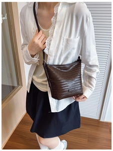 Detail of dark brown woven textured bucket bag with slim shoulder strap worn by a model