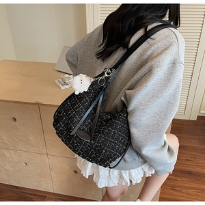 Detail of black tweed tote bag featuring golden hardware and a white plush keychain