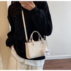 White minimalist crossbody bag with gold lettering and cute plush ball charm