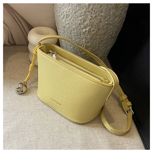 Close-up of bright yellow litchi grain leather bag with heart-shaped metal pendant charm